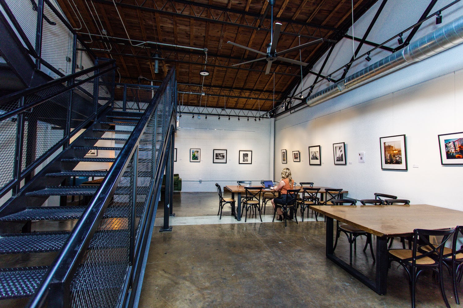 Large commercial ceiling fan installed in a space with tables, stairs, and artwork on the walls